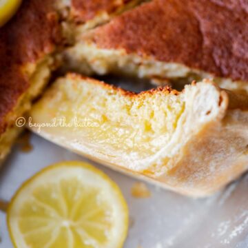 Close up of lemon sponge pie with one slice on its side paired with a slice of lemon below it | All Images © Beyond the Butter®