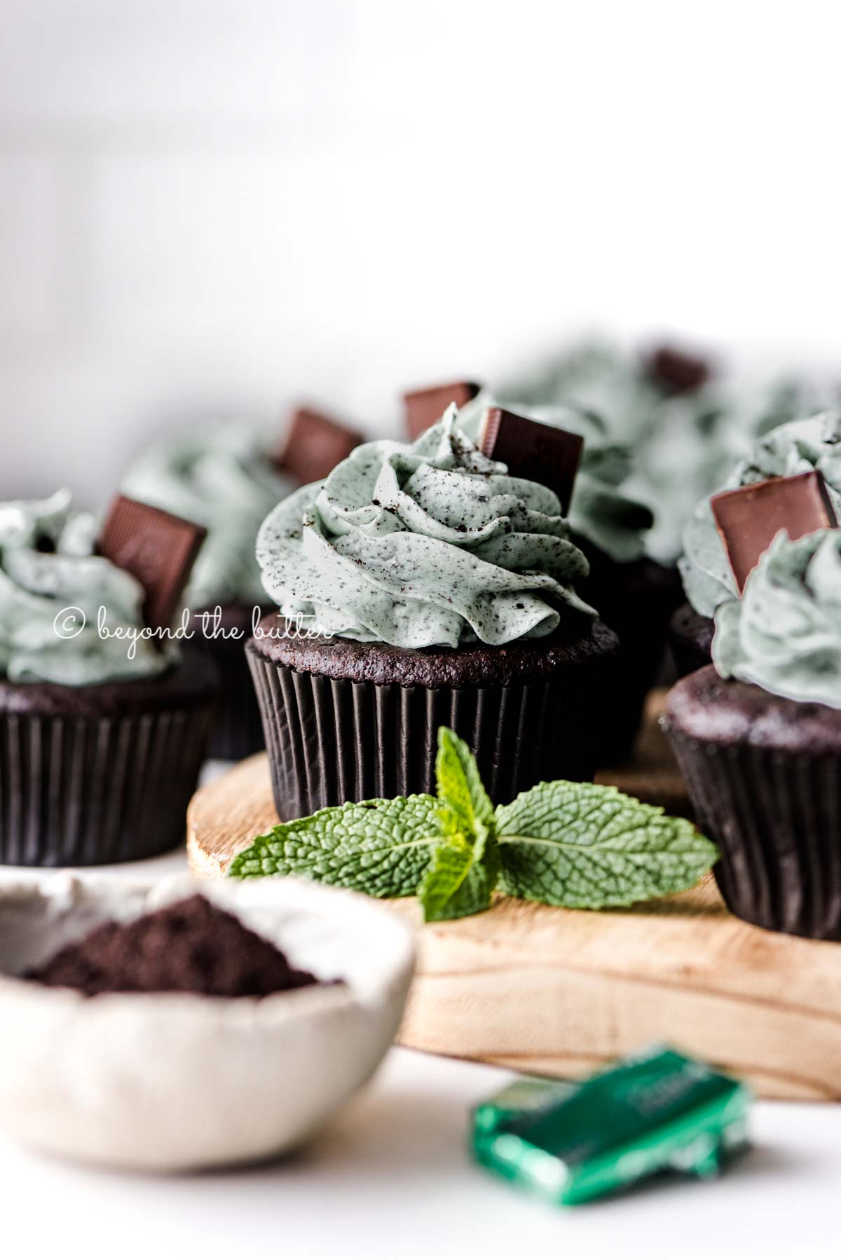 Mint chocolate cupcakes on a wood circular tray with mint leaves as decoration | All Images © Beyond the Butter®