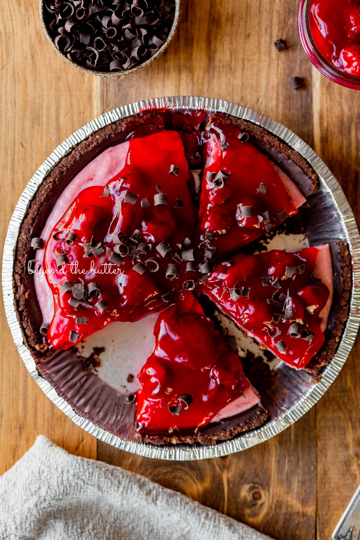 No bake strawberry chocolate pie with small bowl of chocolate curls and extra strawberry pie filling on wood table | All images © Beyond the Butter®