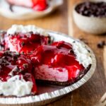 Sliced no bake strawberry chocolate cream pie on wood table with a fork and small bowl of chocolate curls nearby.