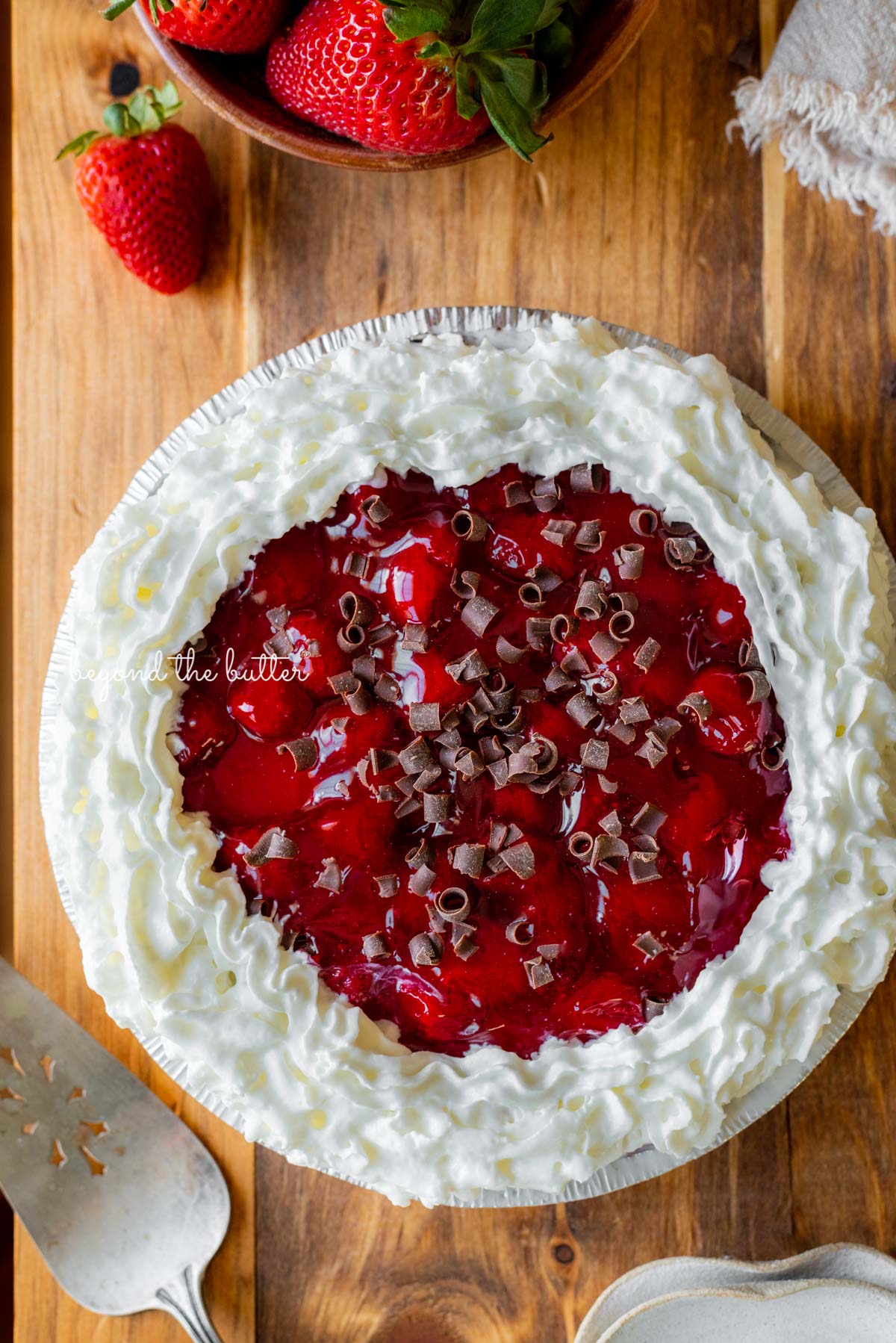 Decorated no bake strawberry chocolate pie with small bowl of strawberries, dessert plates, and pie server on wood table | All images © Beyond the Butter®