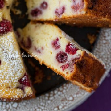 Sliced lemon raspberry ricotta cake on crackled ceramic cake stand and purple wood background | © Beyond the Butter®