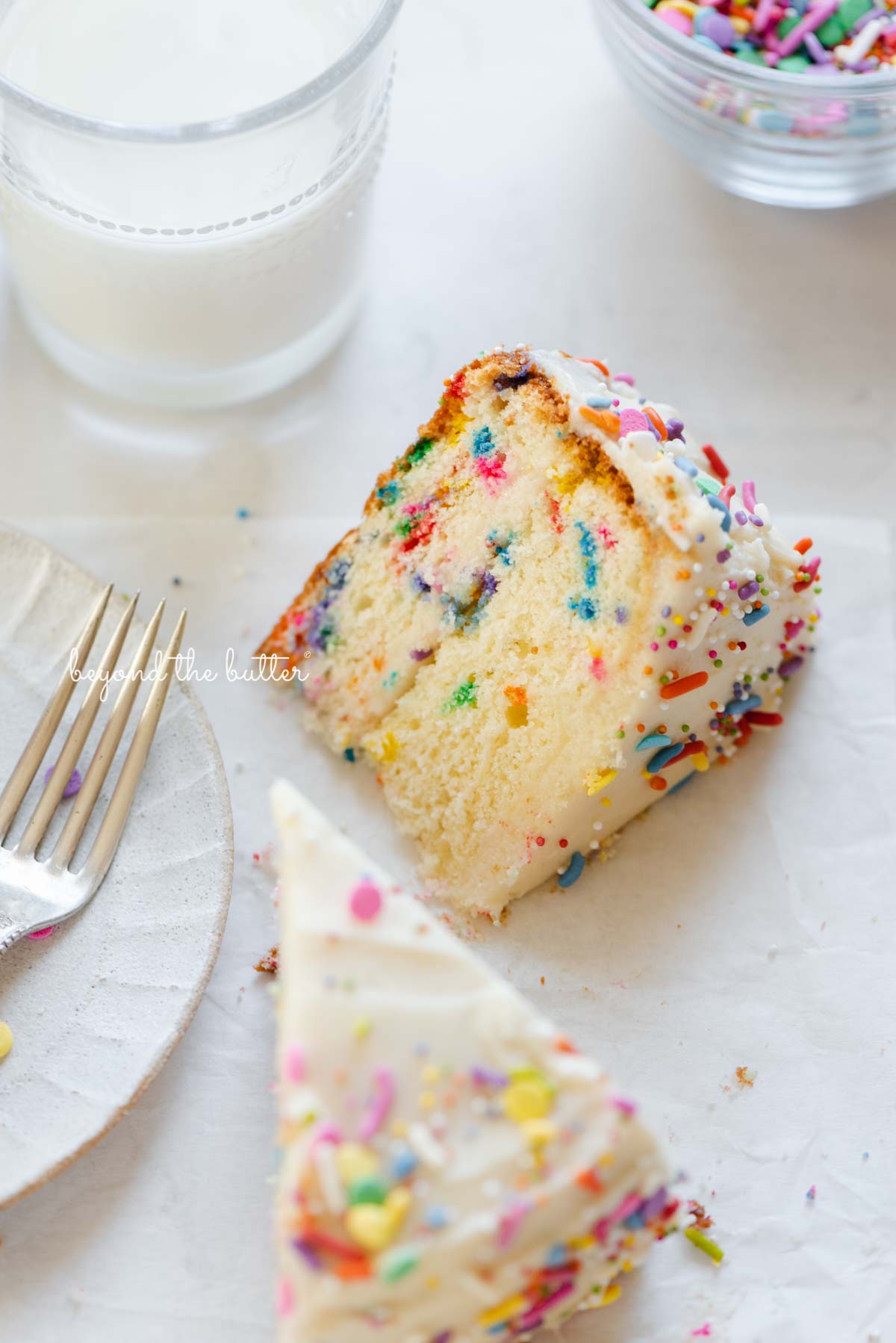 Slices of single layer funfetti cake on their side with a dessert plate, small fork, and glass of milk nearby from BeyondtheButter.com | All images © Beyond the Butter®
