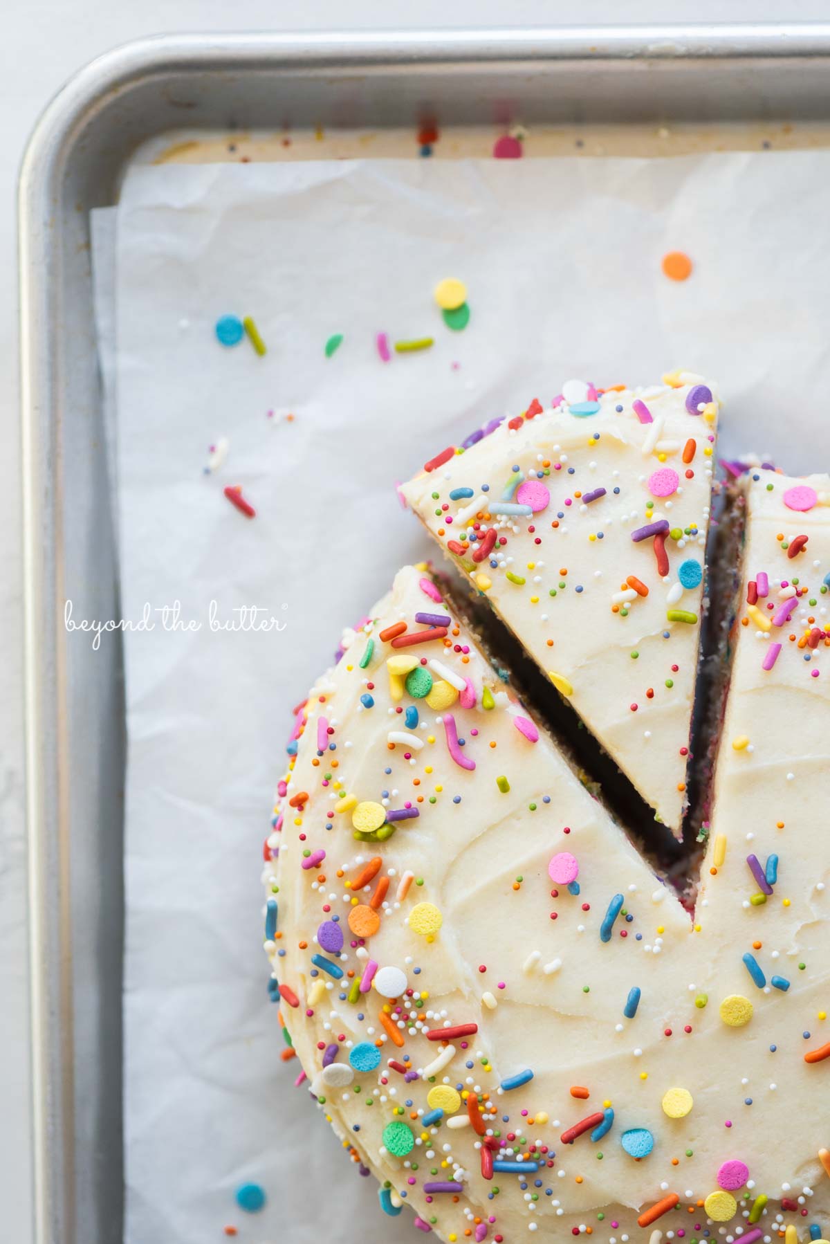 Cut slice of single layer funfetti cake partially removed from rest of the cake on a parchment paper lined baking sheet | All images © Beyond the Butter®