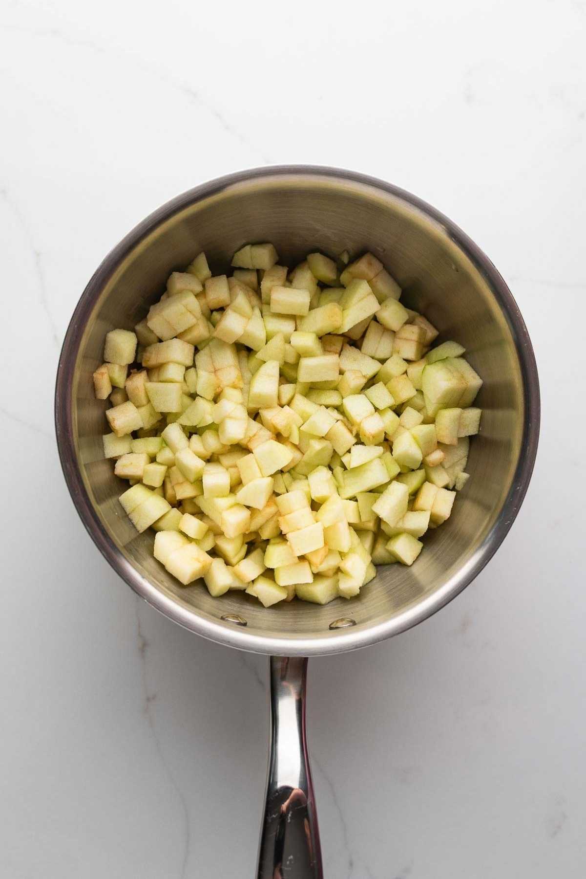 Peeled and chopped apples in a medium saucepan on a light grey marbled background.