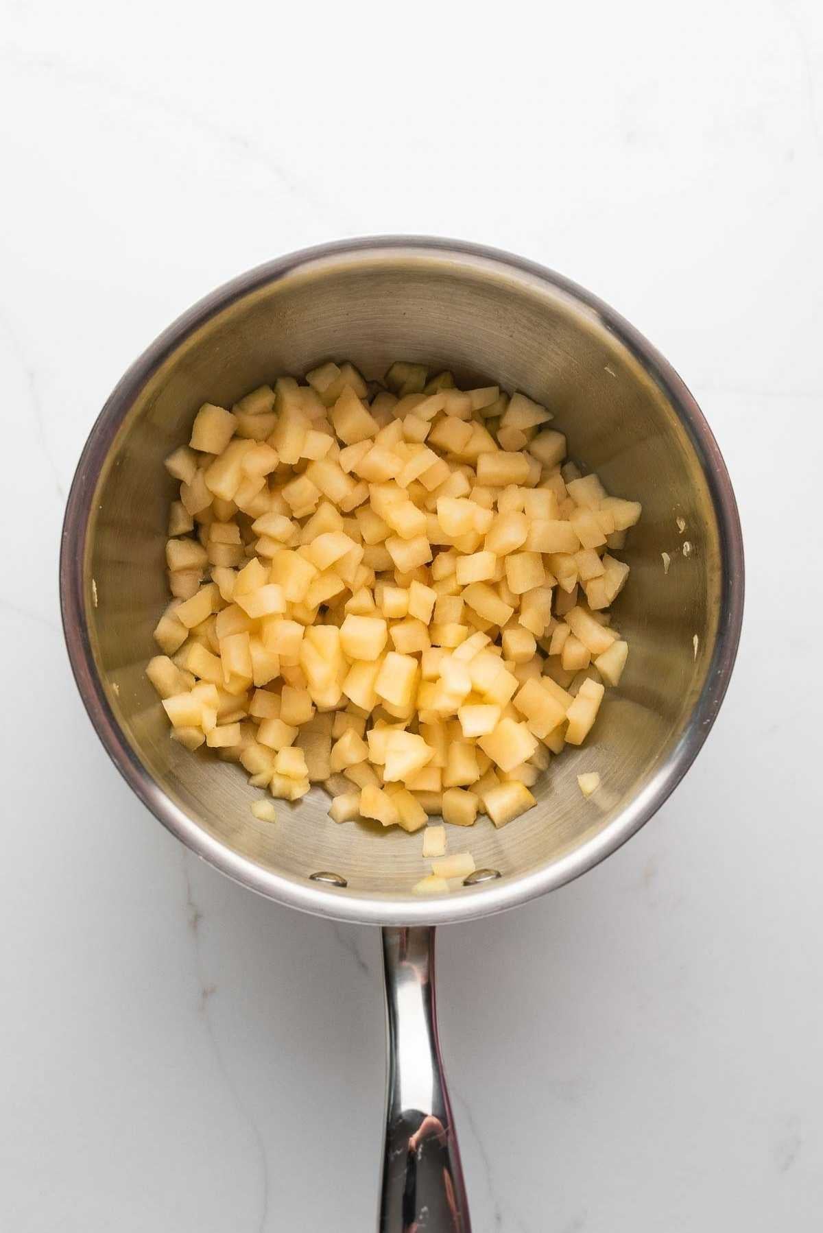 Cooked and softened apples in a medium saucepan on a light grey marbled background.