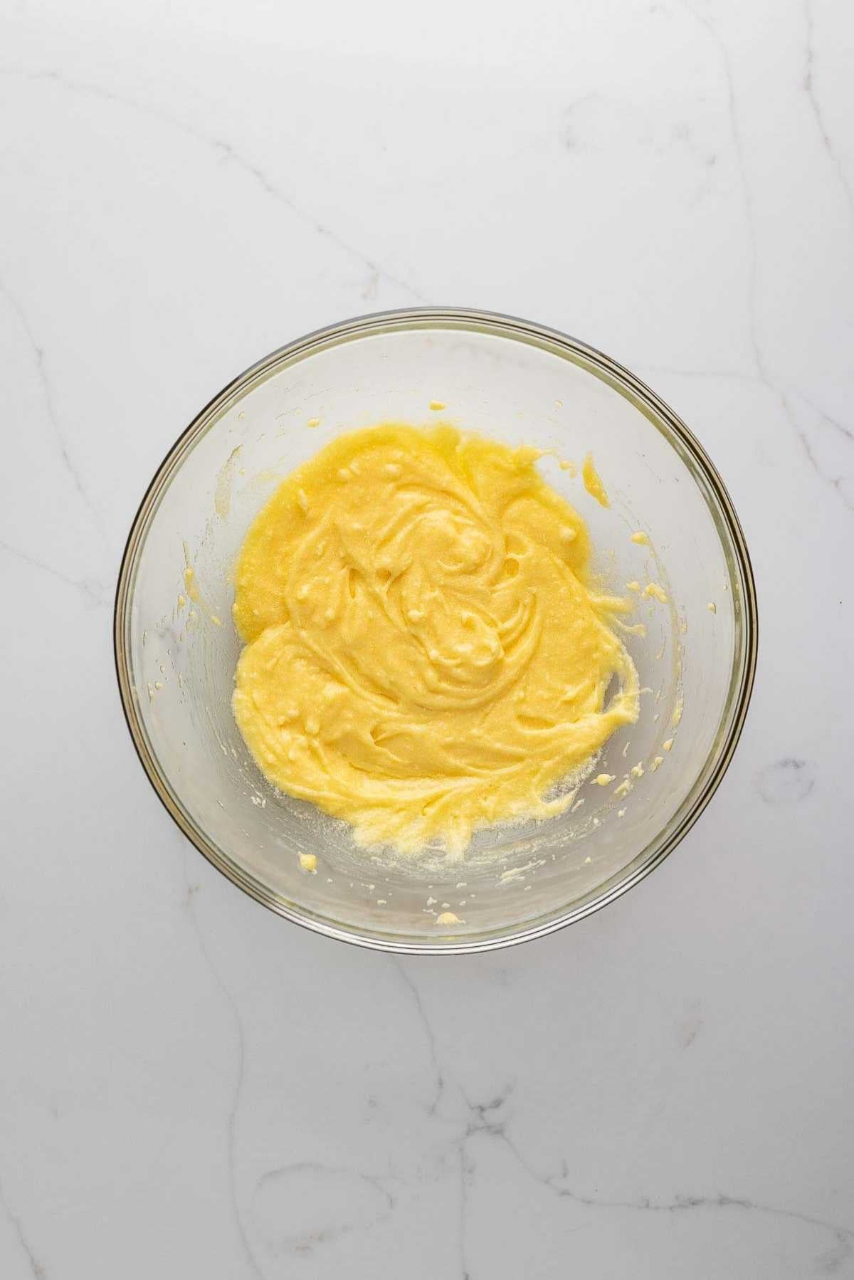 Butter, egg, sugar, and salt whisked together in a glass mixing bowl on a light grey marbled background.