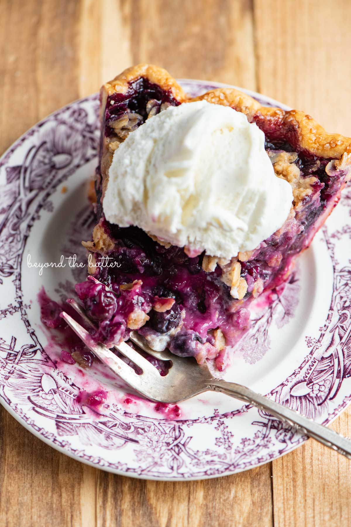 Half eaten slice of blueberry crumble pie with scoop of vanilla bean ice cream on top | © Beyond the Butter®