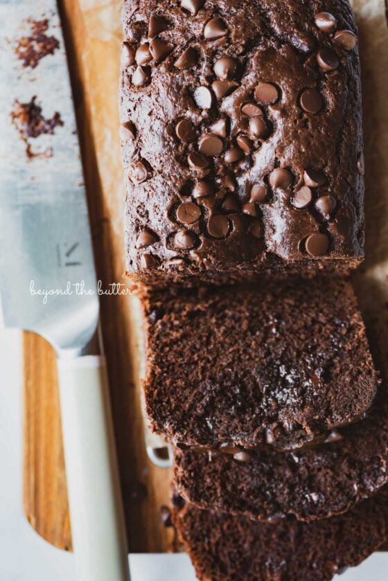 Sliced chocolate zucchini bread on a cutting board with a knife | © Beyond the Butter®