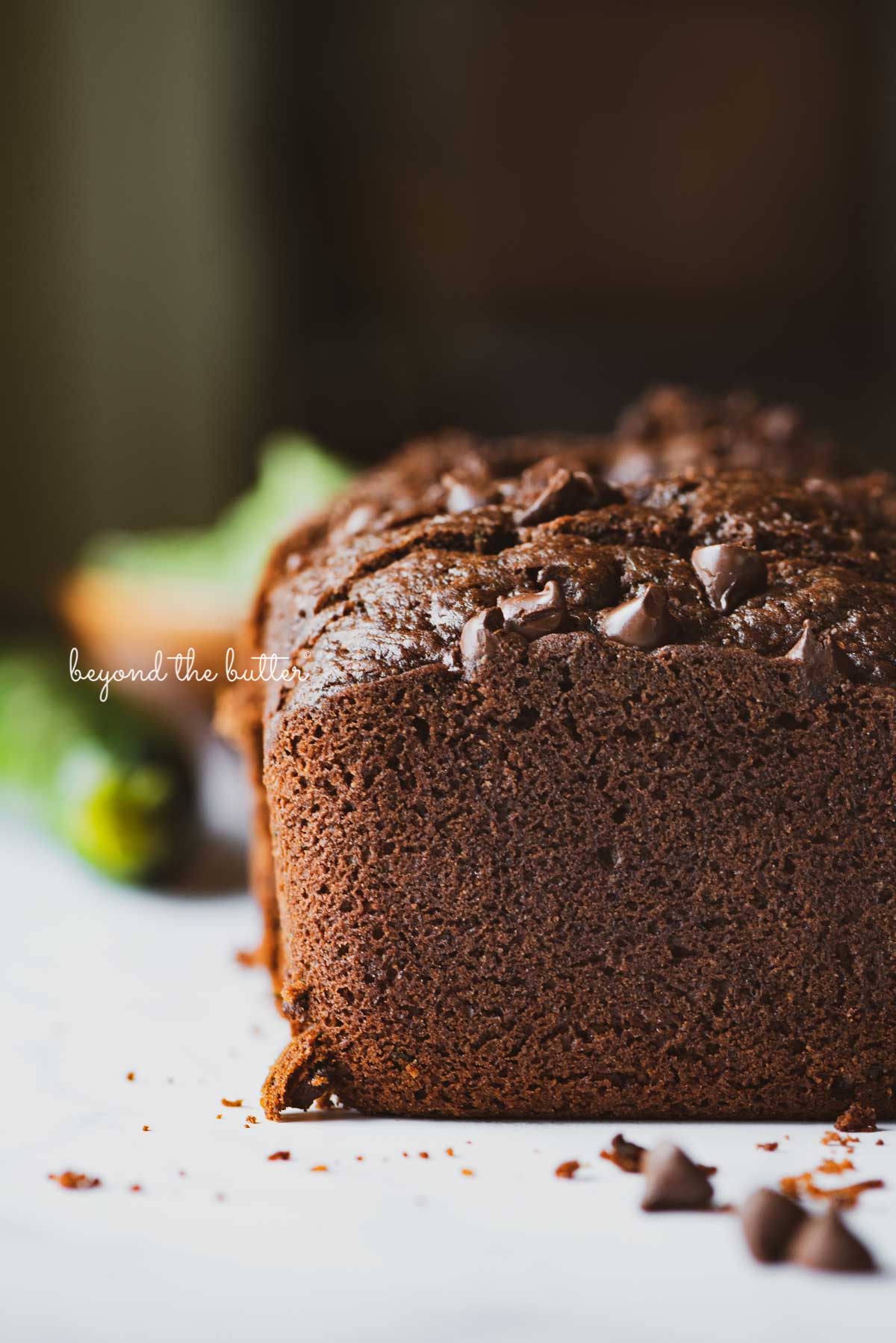 Sliced chocolate zucchini bread with fresh zucchini in the background | © Beyond the Butter®