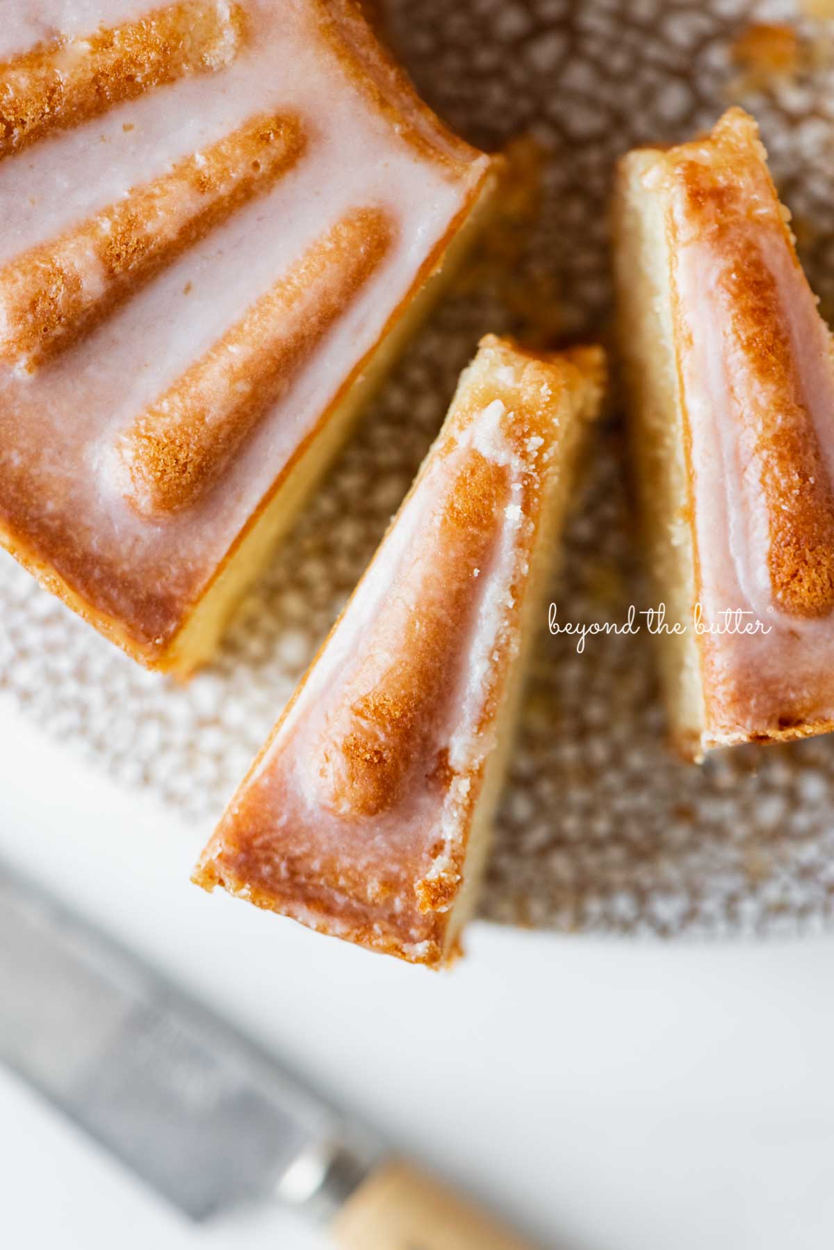 Sliced lemon cream cheese pound cake with a lemon glaze on a cake stand | © Beyond the Butter®