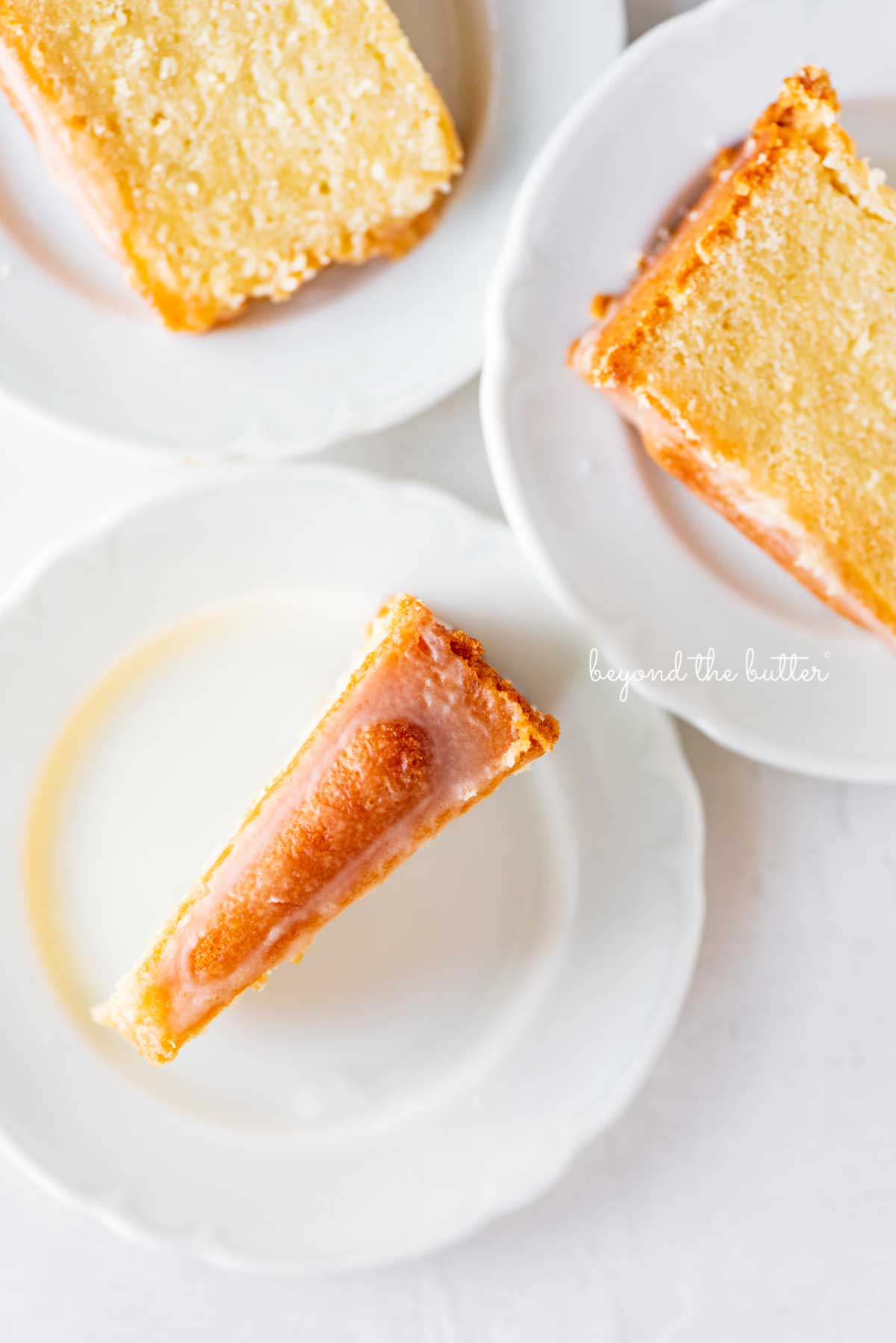 Slices of lemon cream cheese pound cake on small white dessert plates | © Beyond the Butter®