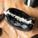 Half eaten oreo macaron on parchment paper surrounded by oreo macarons and broken pieces of oreo cookies.