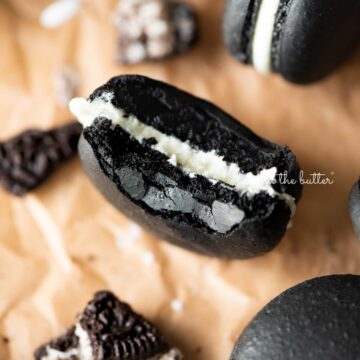 Half eaten oreo macaron on parchment paper surrounded by oreo macarons and broken pieces of oreo cookies | © Beyond the Butter®