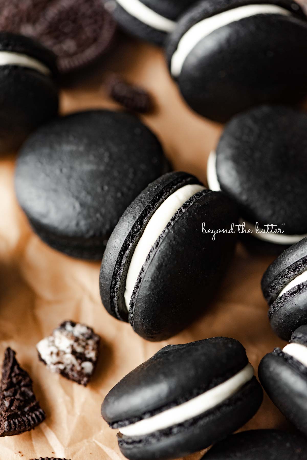 Oreo macarons on parchment paper with broken pieces of oreo cookies nearby | © Beyond the Butter®