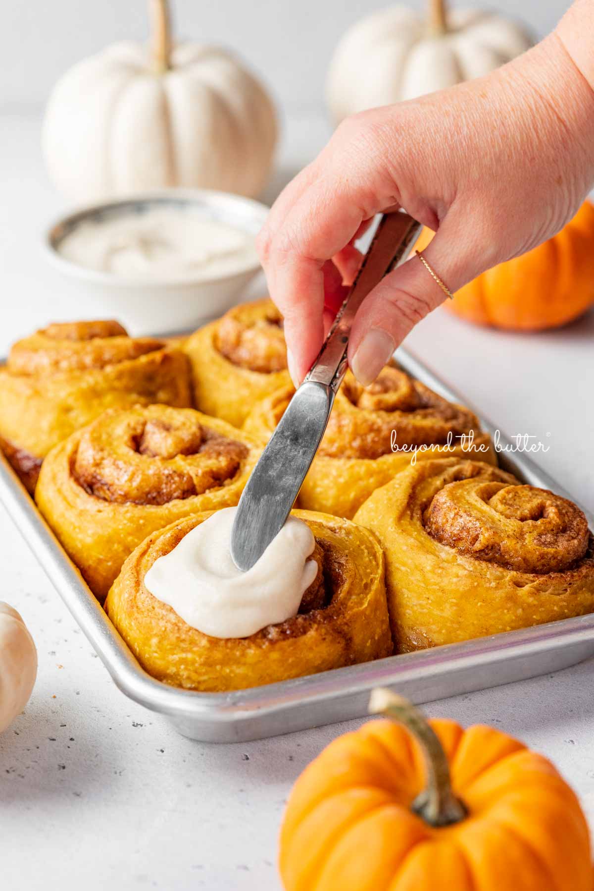 Applying the maple frosting to the tops of each pumpkin cinnamon roll | © Beyond the Butter®