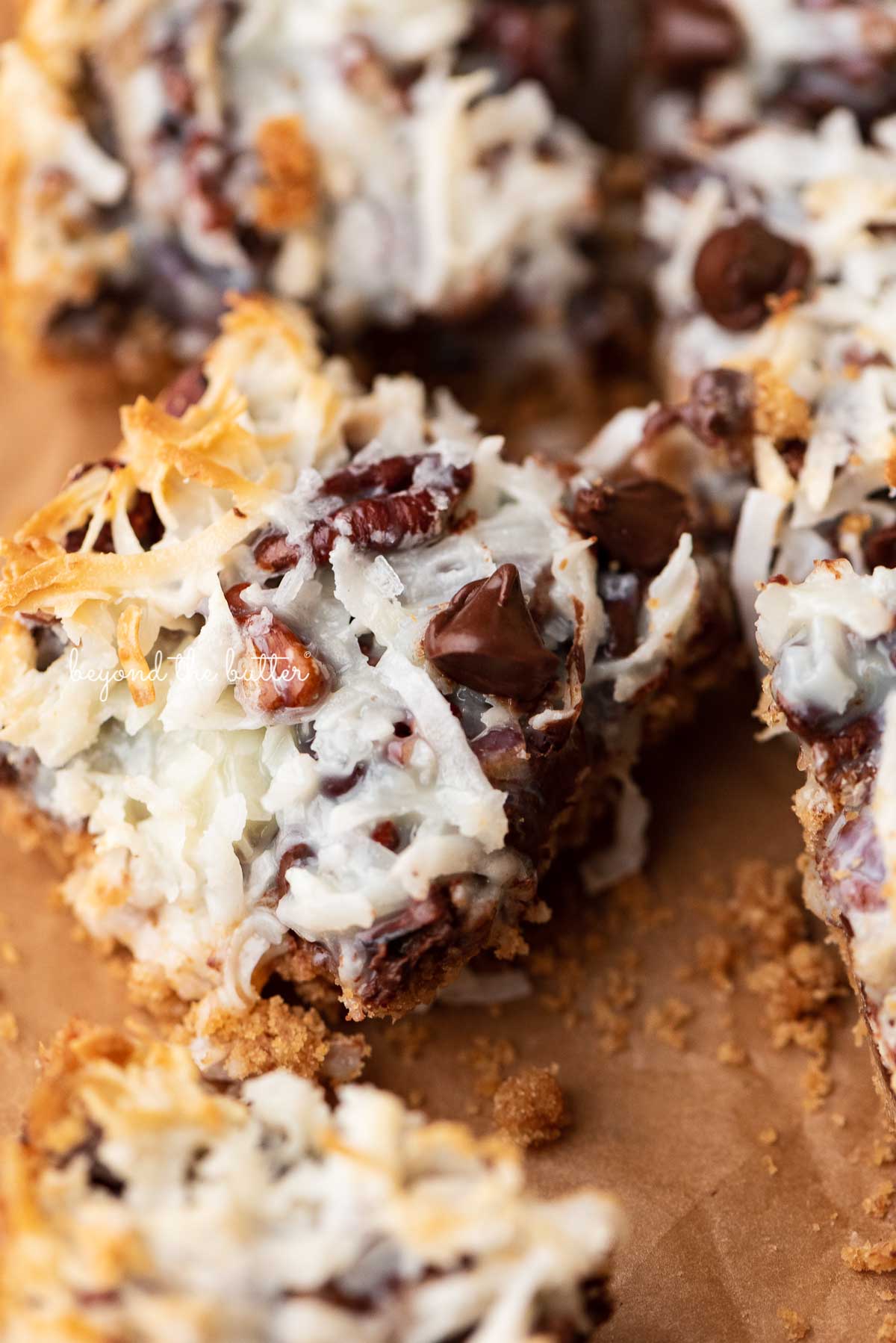 7 layer magic cookie bars on brown parchment paper | © Beyond the Butter®