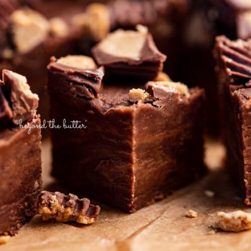 Close up of 1 inch cubes of homemade chocolate peanut butter fudge on brown parchment paper.