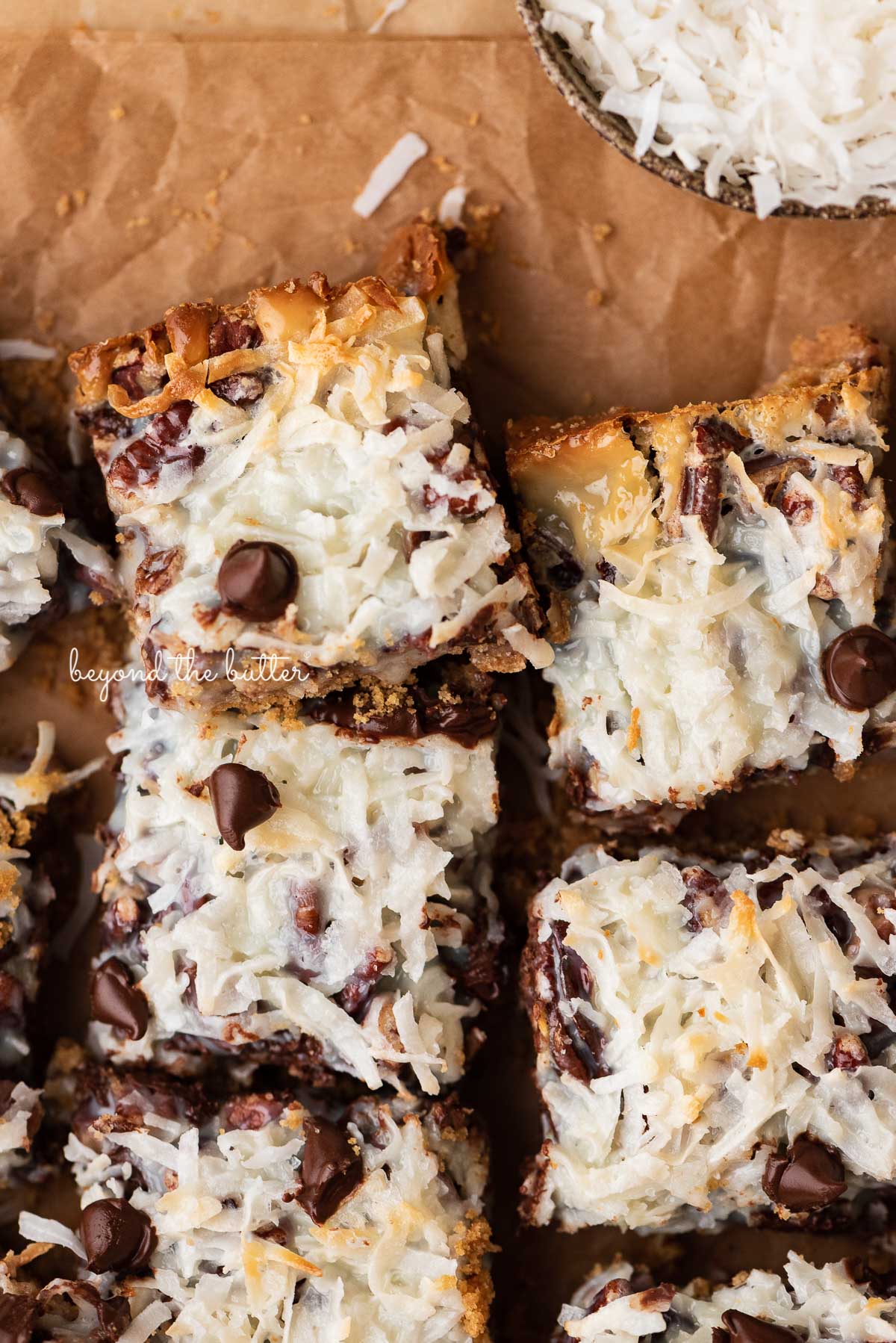 7 layer magic cookie bars on brown parchment paper | © Beyond the Butter®