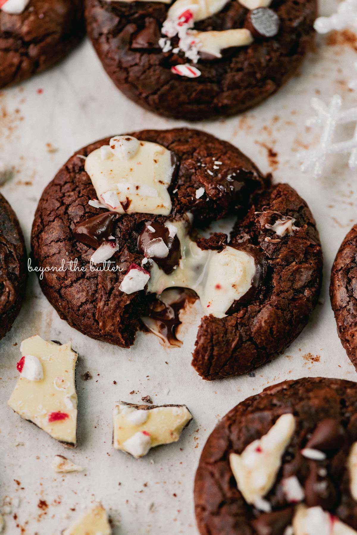 A split peppermint bark brownie crinkle cookie on a parchment paper lined baking sheet | © Beyond the Buter®