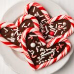 Close up of candy cane hearts on dessert plate on white wood background.