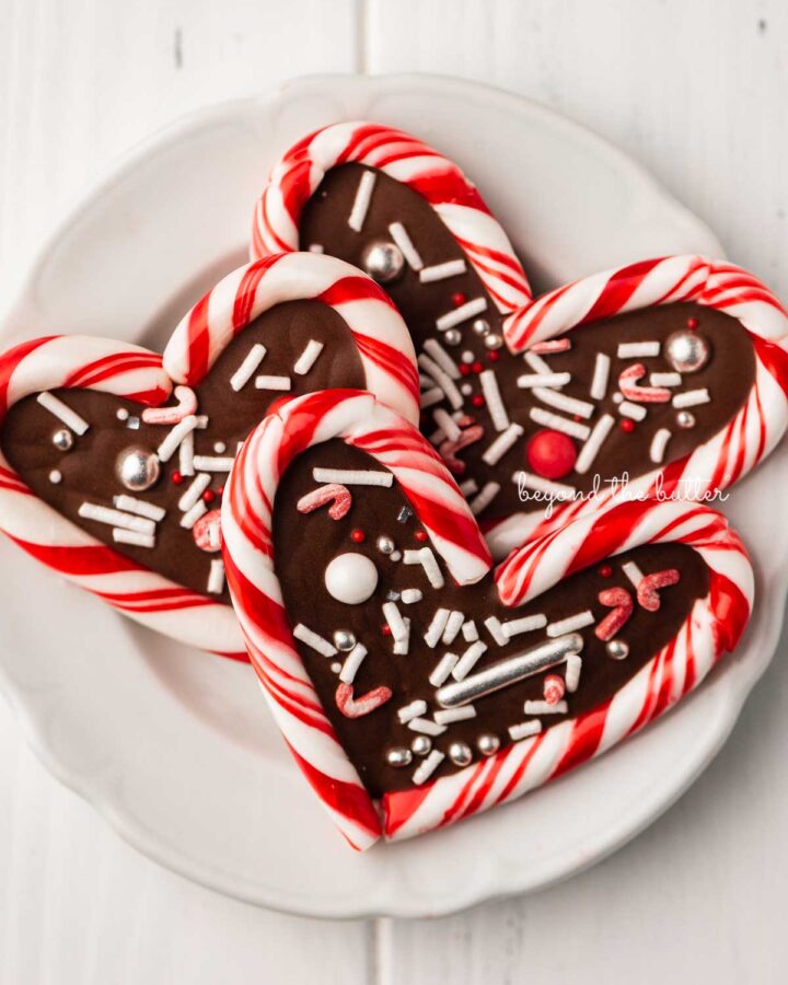 Close up of candy cane hearts on dessert plate on white wood background.