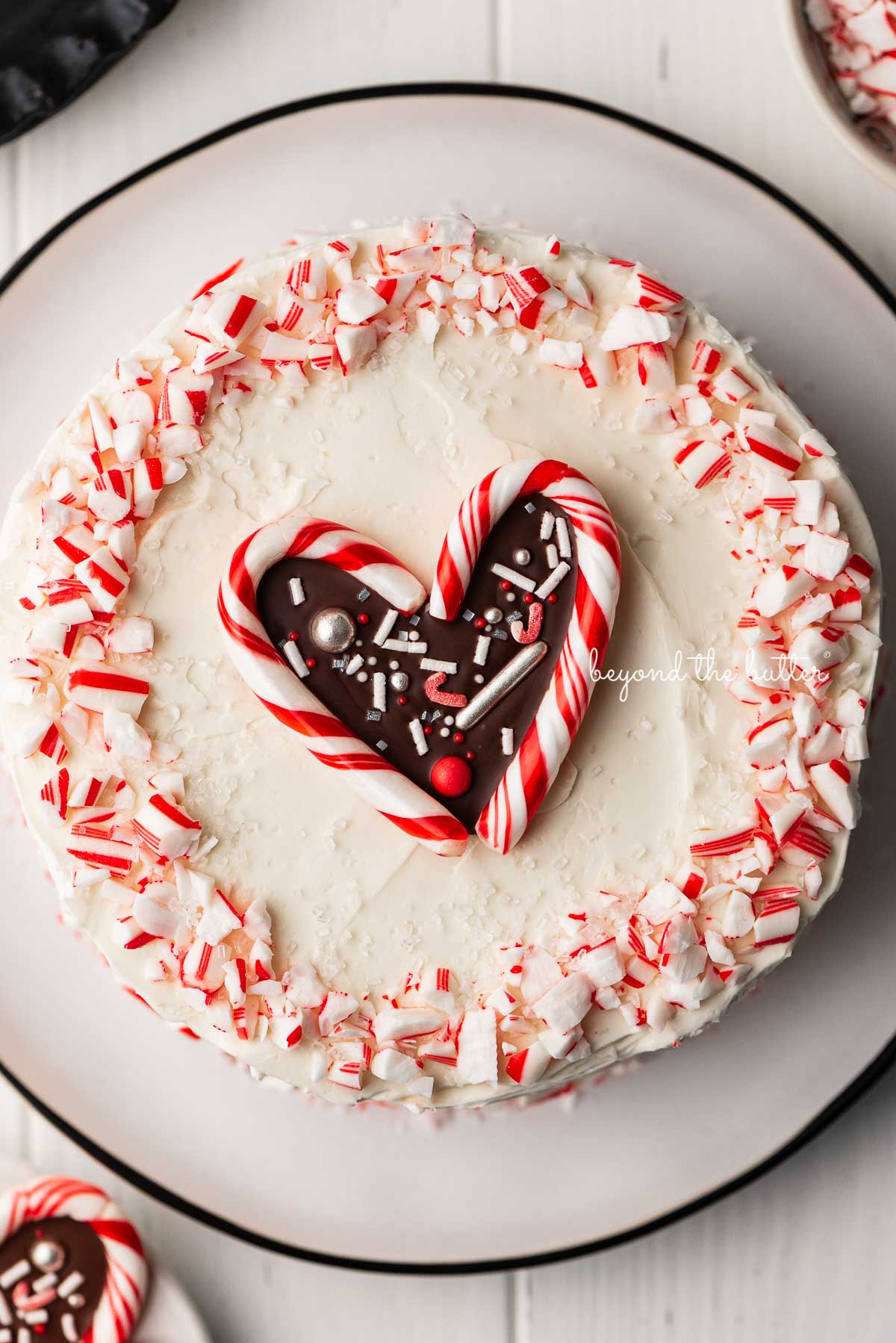 Single layer chocolate peppermint cake frosted with peppermint swiss merignue buttercream and garnished with crushed candy canes and candy cane heart | © Beyond the Butter®