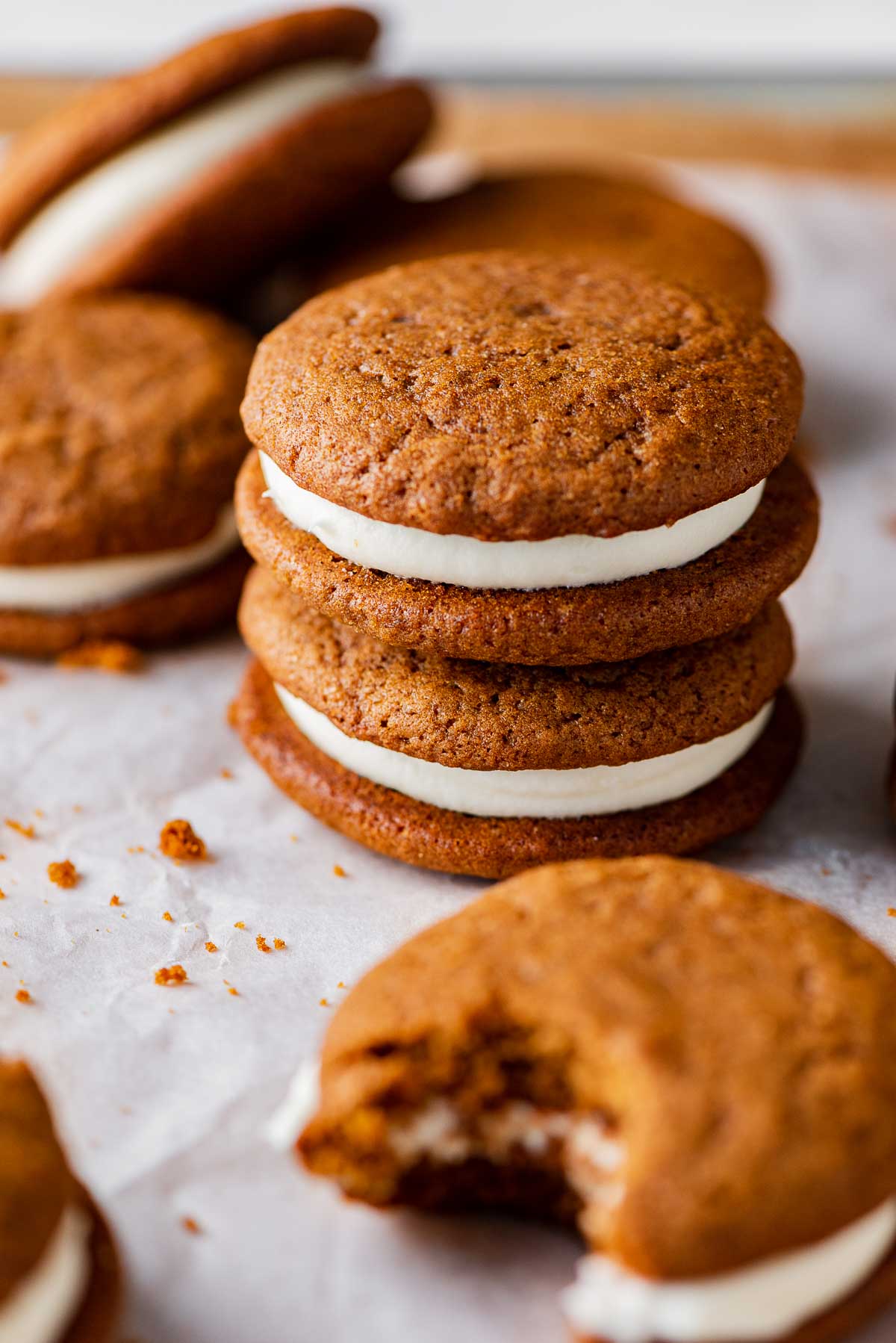 Stacked gingerbread whoopie pies filled with cream cheese frosting on a parchment paper lined baking sheet | © Beyond the Butter®