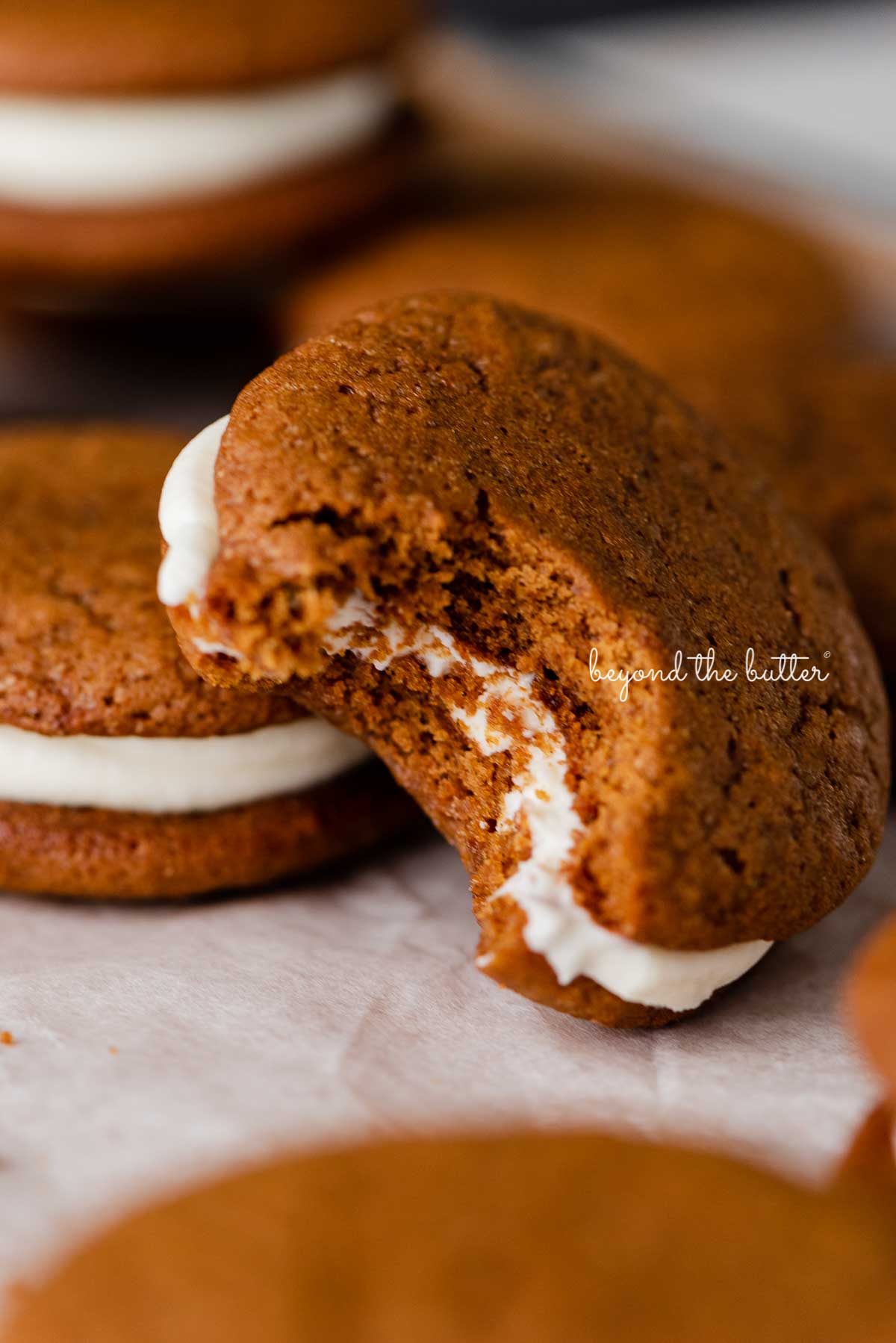 Half eaten homemade gingerbread whoopie pie stacked with more whoopie pies on parchment paper | © Beyond the Butter®