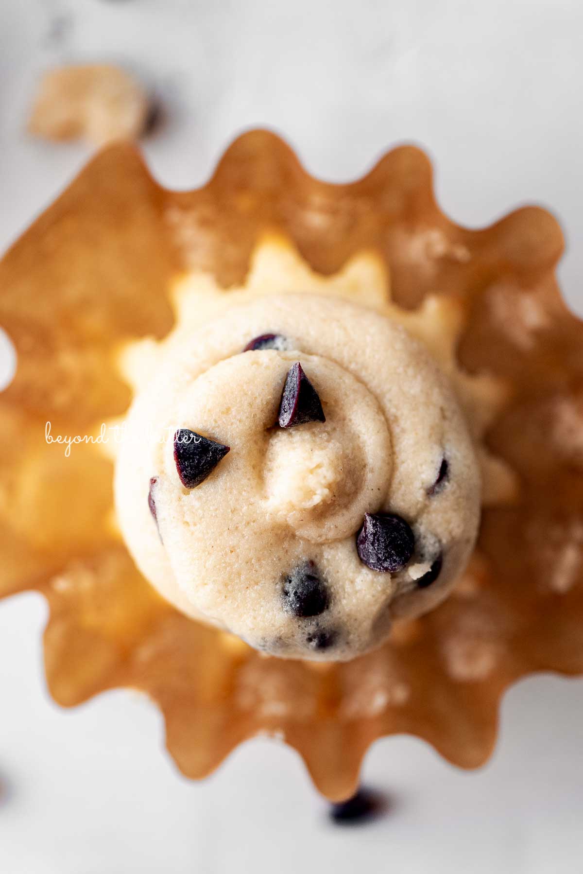 An opened chocolate chip cookie dough cupcake on a white marbled background | © Beyond the Butter®