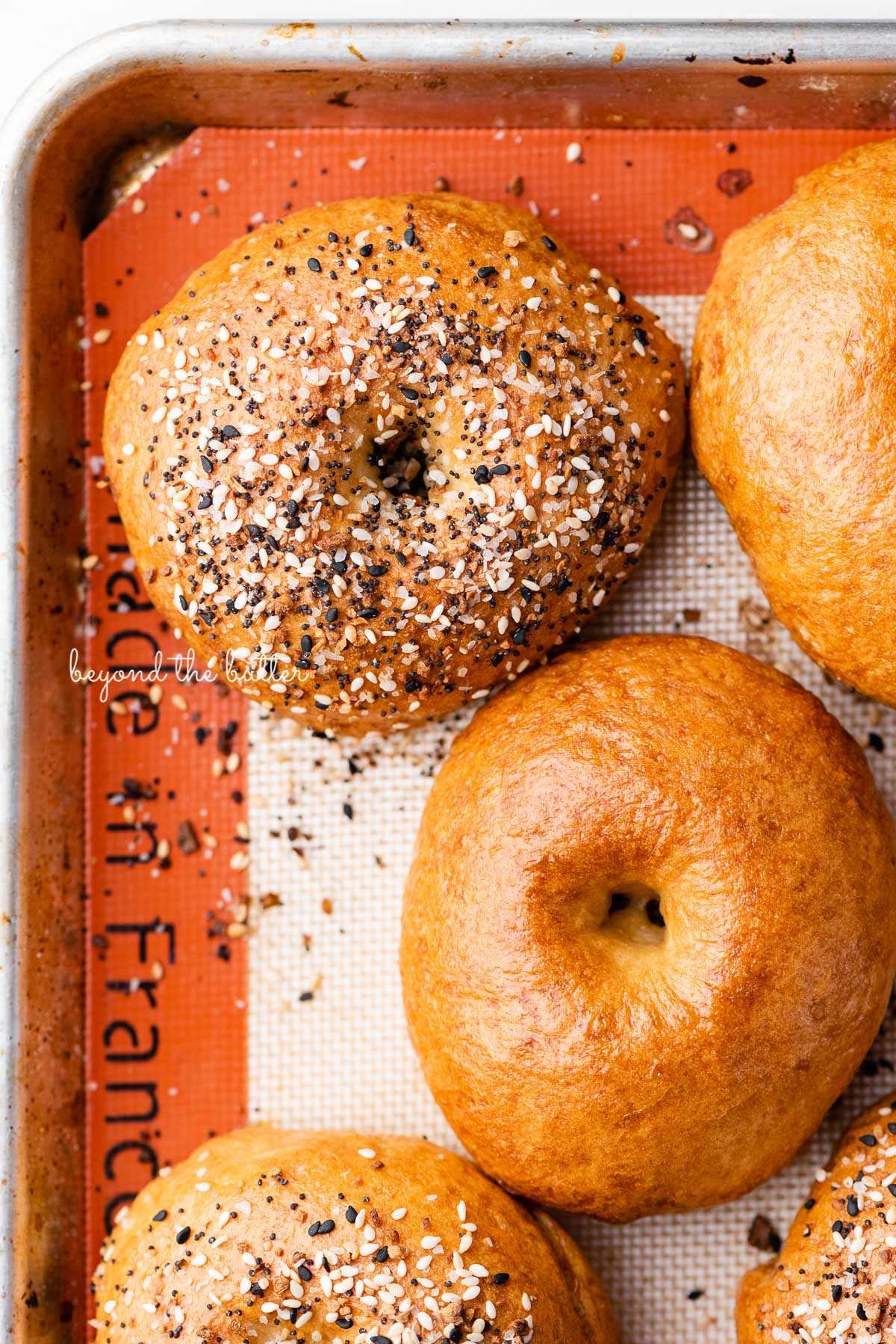 Silicone mat lined baking sheet with just baked homemade bagels | © Beyond the Butter®
