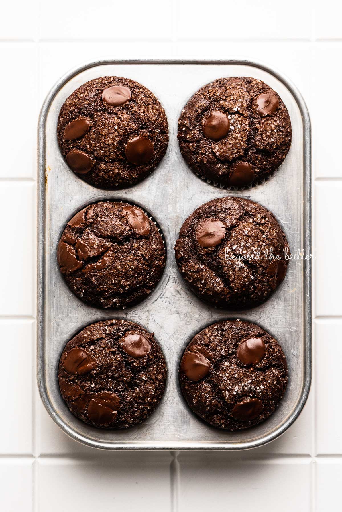 Double chocolate chip muffins in vintage muffin tin on white tiled background | © Beyond the Butter®