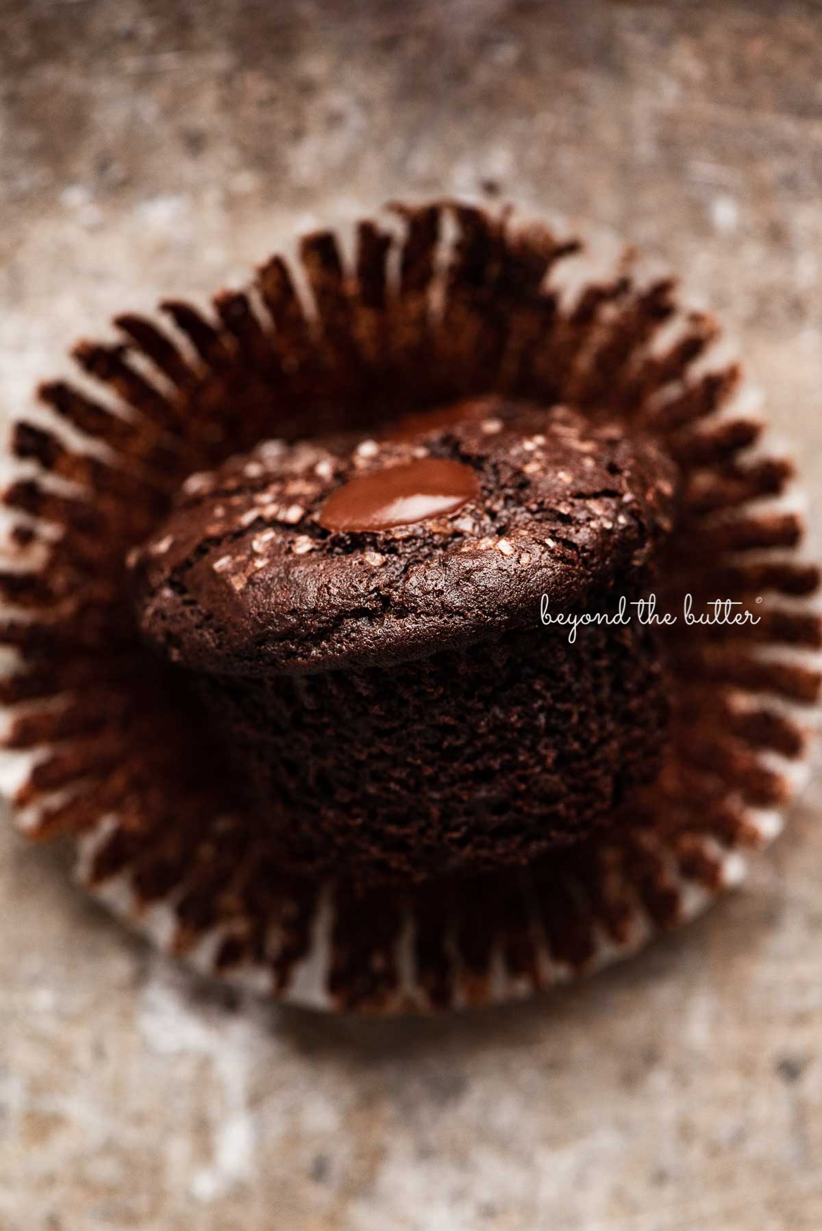 One double chocolate chip muffin without the liner on it's side on light vintage gray background | © Beyond the Butter®
