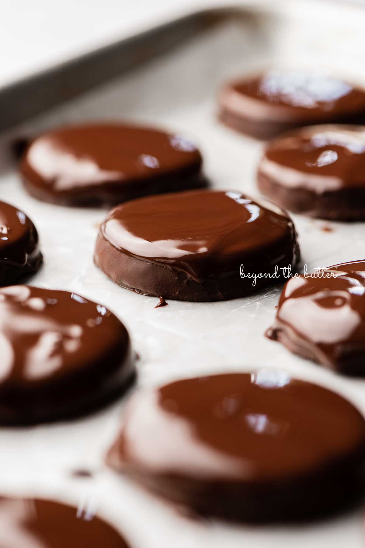 Homemade thin mints double dipped in chocolate on a wax paper lined baking sheet | © Beyond the Butter®