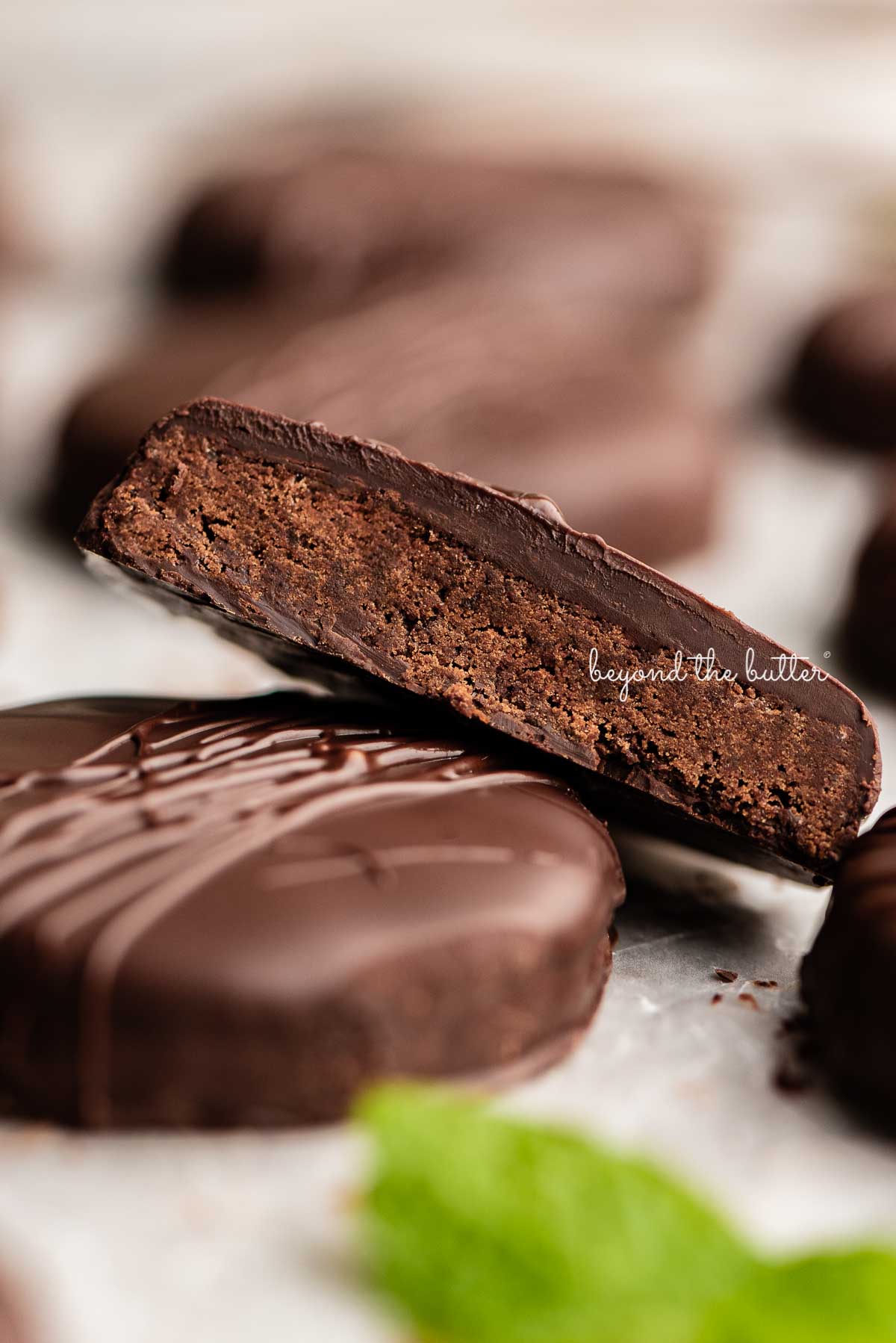 Homemade thin mints on a wax paper lined baking sheet with center cookie cut in half | © Beyond the Butter®