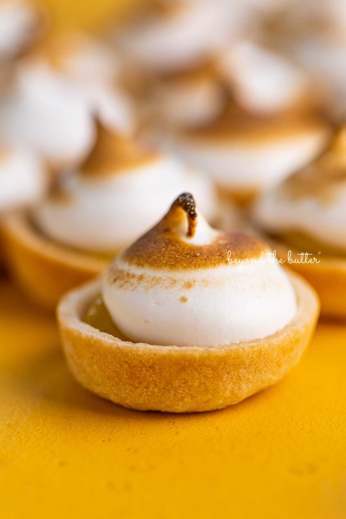 Mini lemon meringue pies on a yellow background | © Beyond the Butter®