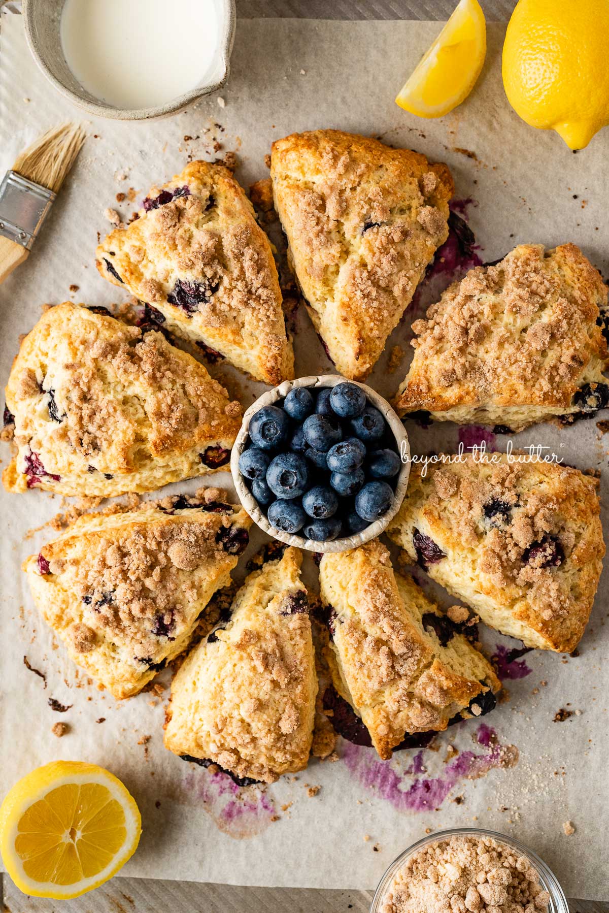 Lemon blueberry streusel scones with a small bowl of blueberries in the center on a parchment lined baking sheet | © Beyond the Butter®