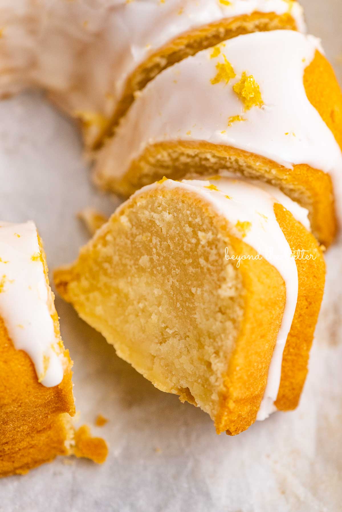 Sliced lemon cream cheese pound cake on white parchment paper | © Beyond the Butter®
