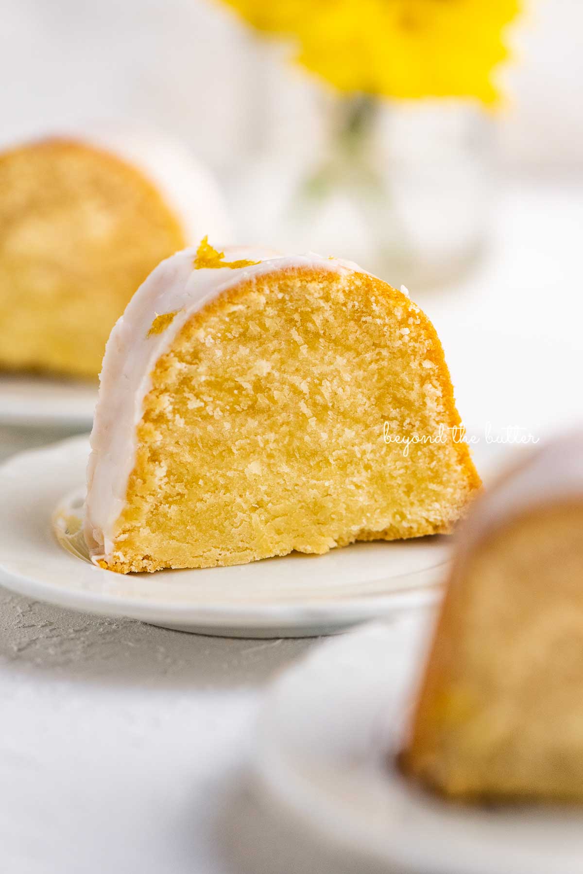 Small lemon cream cheese pound cake slice on a small dessert plate on white background.