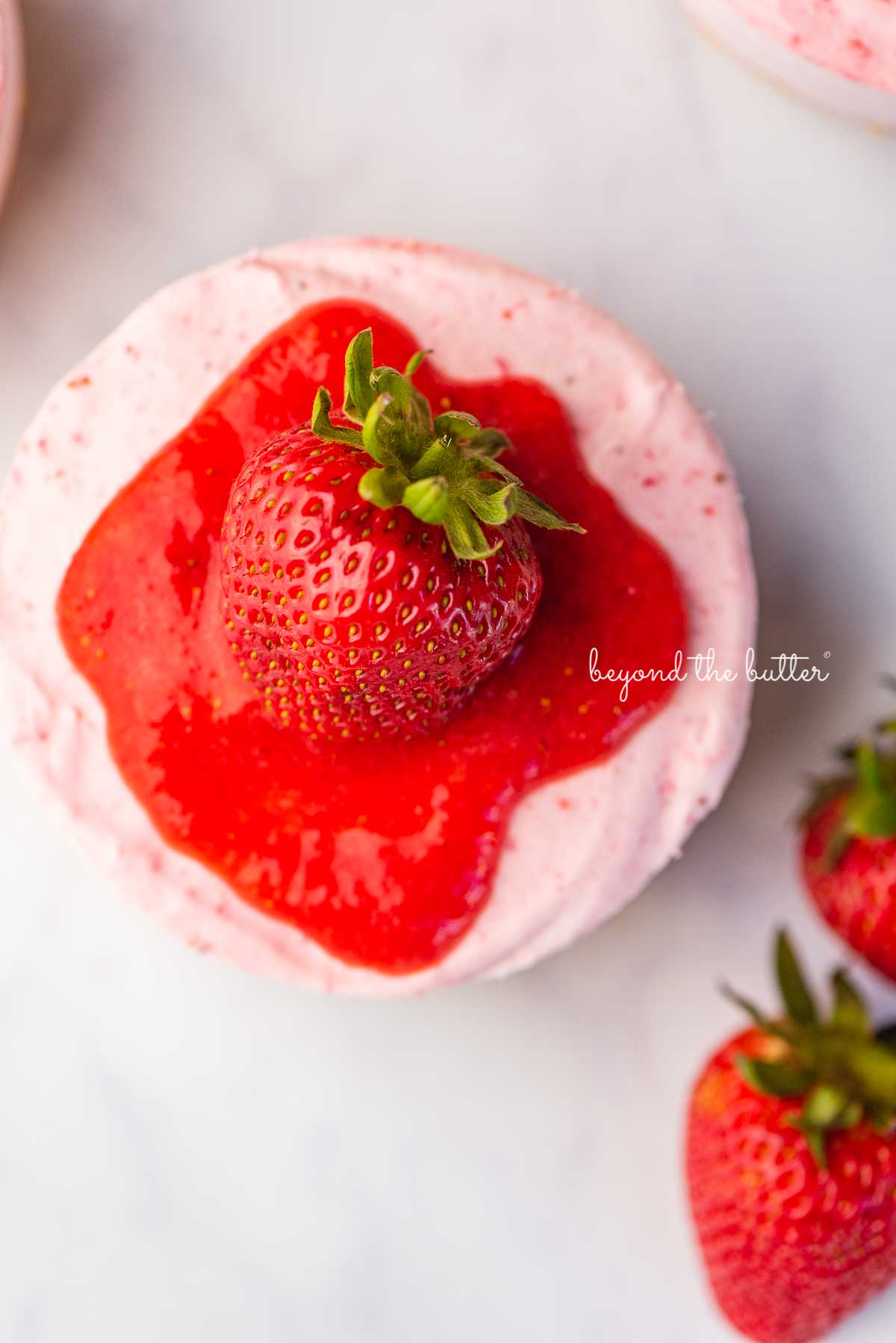 Sliced small 4-inch no-bake strawberry cheesecake on a marbled background | © Beyond the Butter®