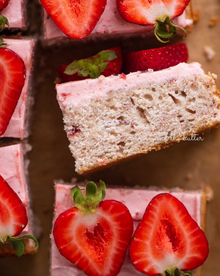 Slices of mini strawberry sheet cake topped with strawberry buttercream frosting and fresh strawberries with one slice on its side.