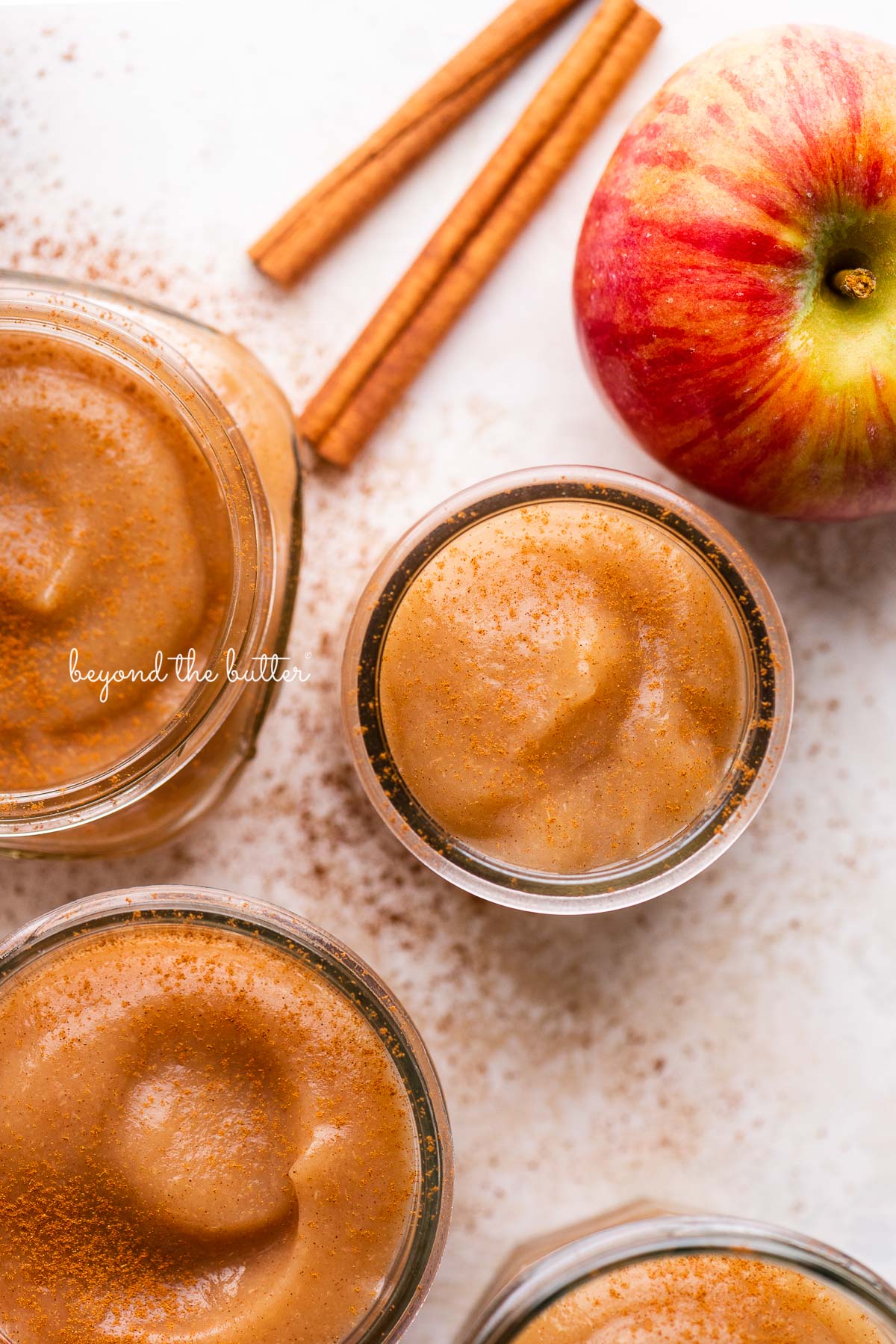 Jars of no sugar added applesauce with cinnamon sticks and apples | © Beyond the Butter®
