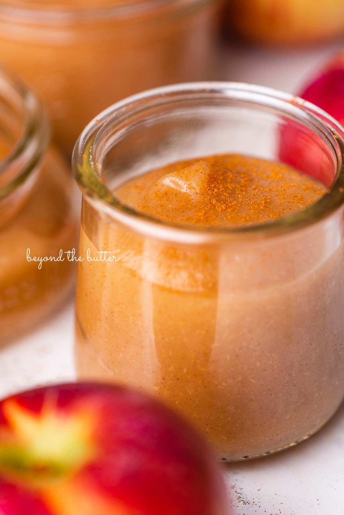 Small jars of no sugar added homemade applesauce with apples next to the jars | © Beyond the Butter®