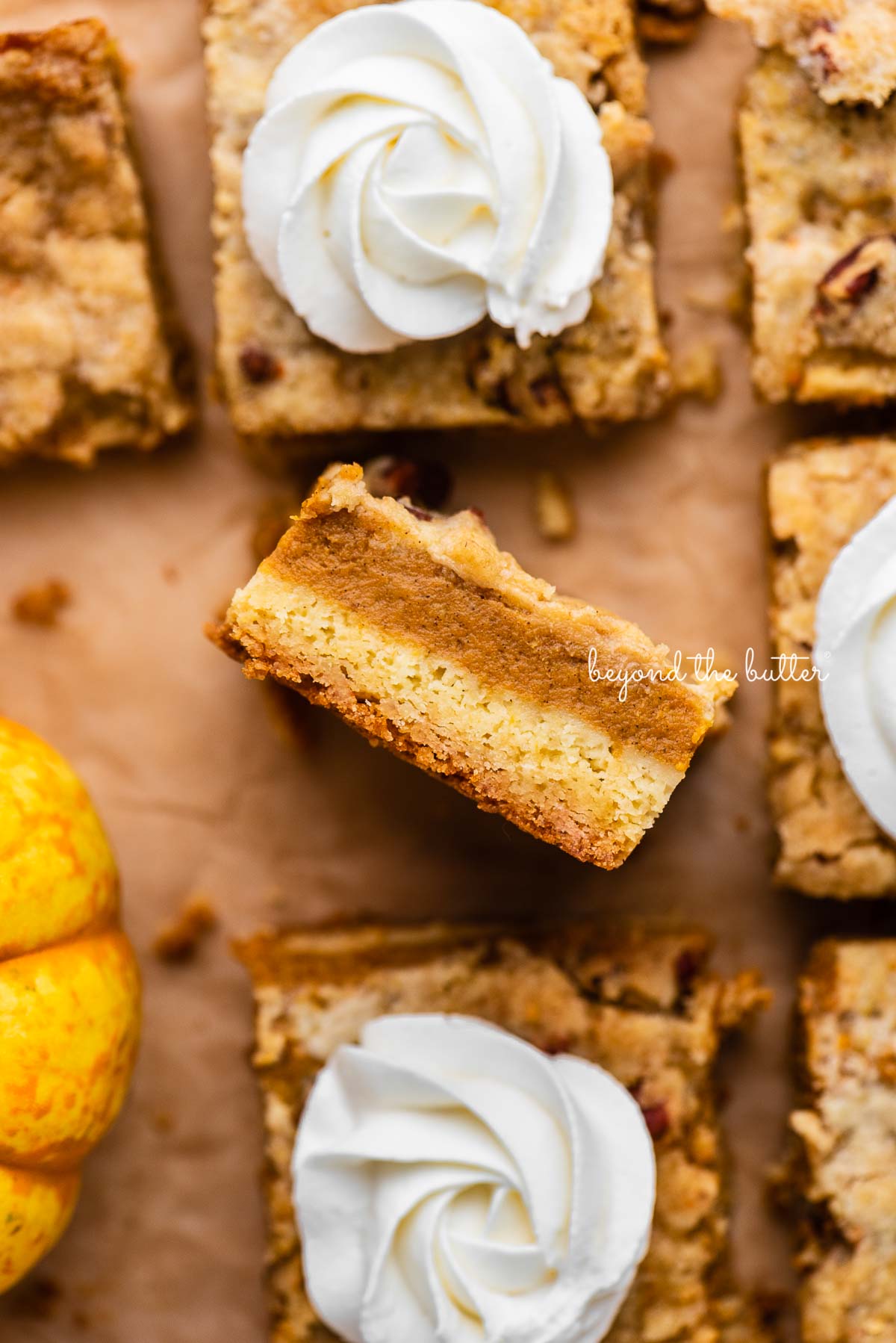Sliced pumpkin pie cake bars on parchment paper background with center slice on its side | © Beyond the Butter®