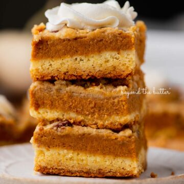 Stack of three pumpkin pie cake bars on a parchment paper lined bottom | © Beyond the Butter®