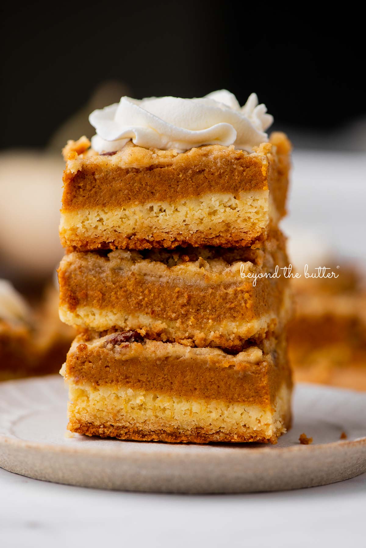 Stack of three pumpkin pie cake bars on a parchment paper lined bottom | © Beyond the Butter®