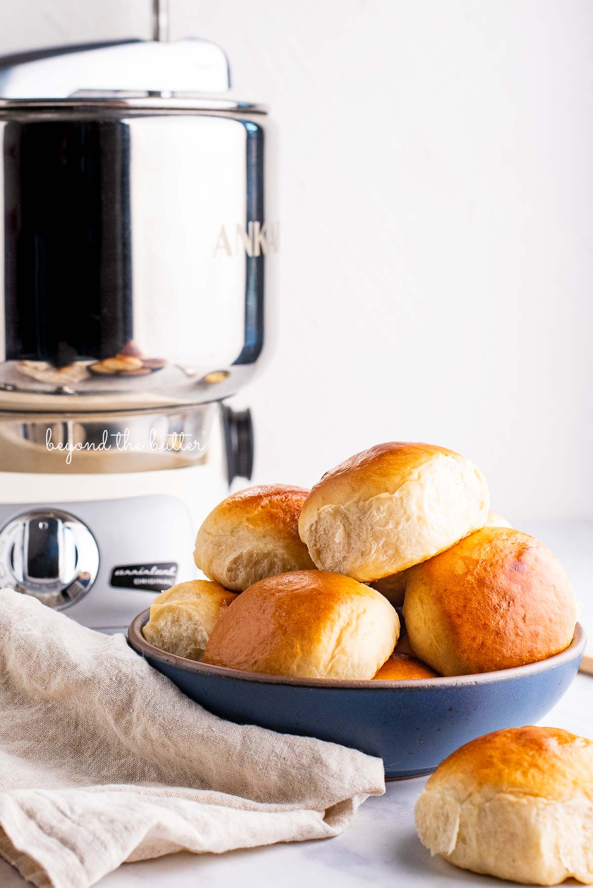 Honey butter dinner rolls in a blue ceramic bowl made with the Ankarsrum Original Mixer | © Beyond the Butter®