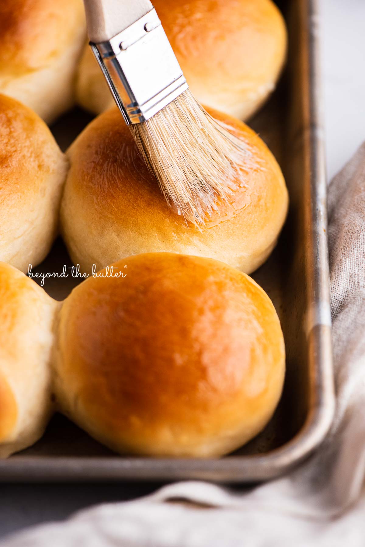 Small tray of honey butter dinner rolls being brushed with more honey butter | © Beyond the Butter®