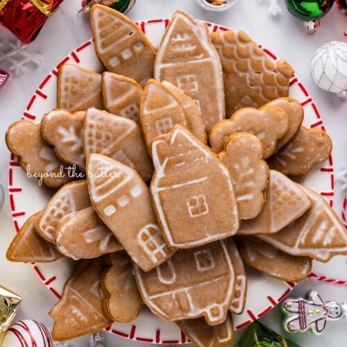 Christmas themed dessert plate filled with soft and chewy gingerbread cookies with ornaments around it on a white marbled background.
