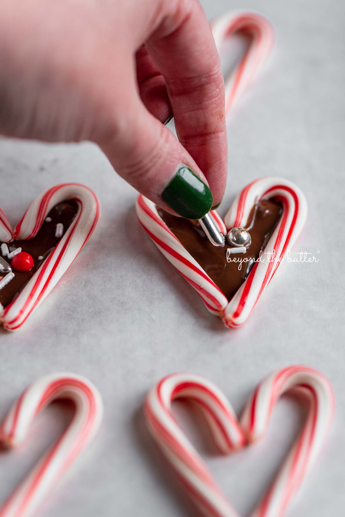 Adding holiday theme sprinkles to candy cane hearts filled with melted chocolate | © Beyond the Butter®